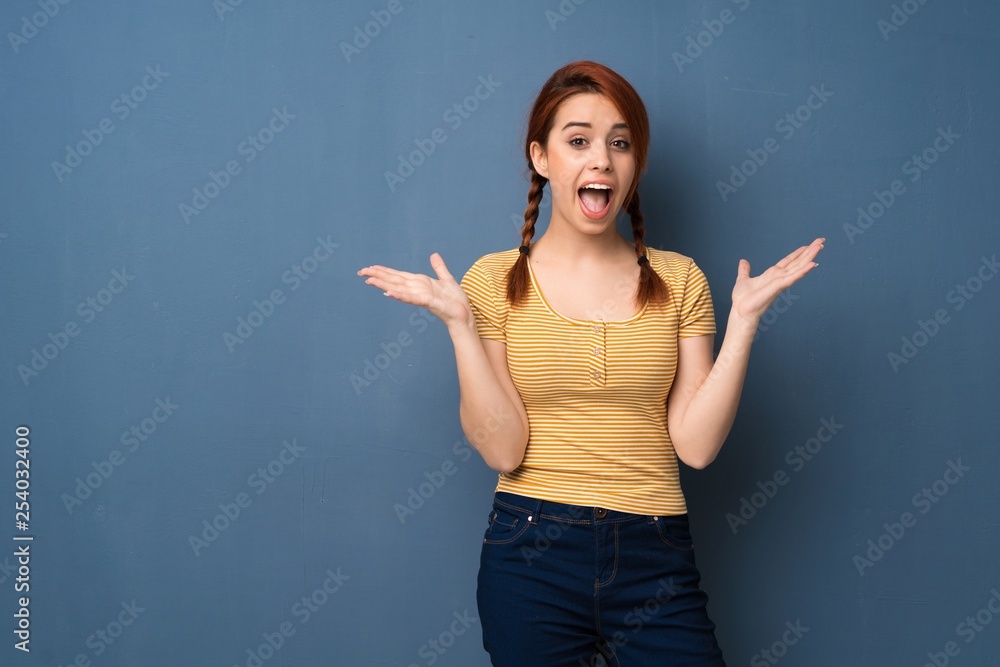 Young redhead woman over blue background with surprise and shocked facial expression Young redhead woman over blue background with surprise and shocked facial expression