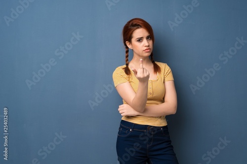 Young redhead woman over blue background making horn gesture © luismolinero
