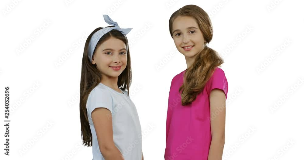 Portrait of the nice teenagers girls smiling while standing face to face on the white background and posing to the camera. Portrait of the nice teenagers girls smiling while standing face to face on the white background and posing to the camera.