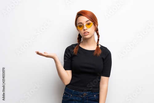 Young redhead woman over white wall holding copyspace with doubts