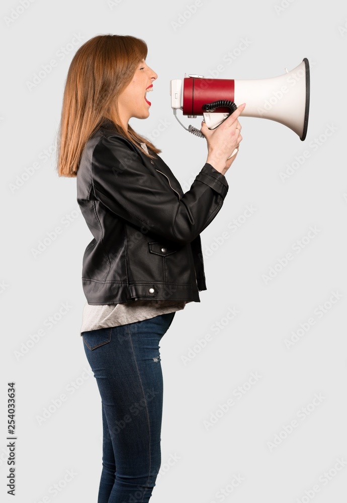 Young redhead woman shouting through a megaphone over isolated grey background