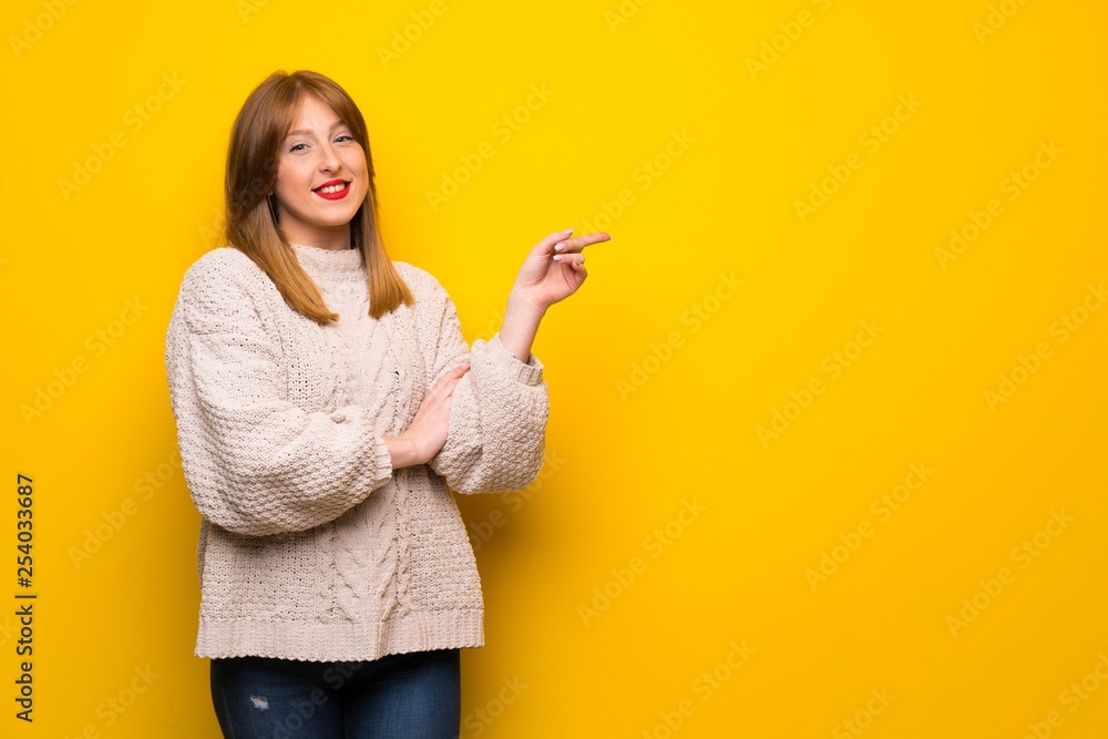 Redhead woman over yellow wall pointing finger to the side Redhead woman over yellow wall pointing finger to the side