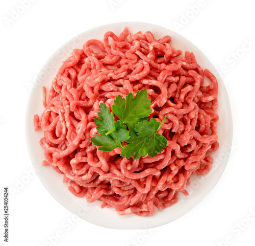 Minced meat in a plate and parsley leaves on a white. The form of the top.