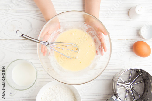 Children's small hands beat the dough for pancakes cooking in the kitchen