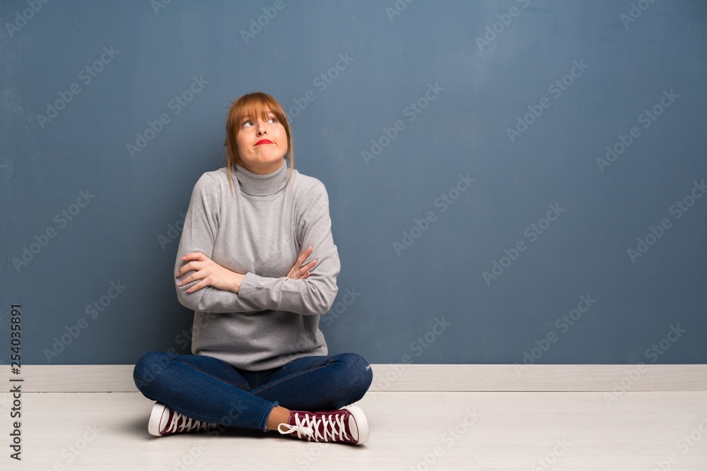Redhead woman siting on the floor making doubts gesture while lifting the shoulders Redhead woman siting on the floor making doubts gesture while lifting the shoulders