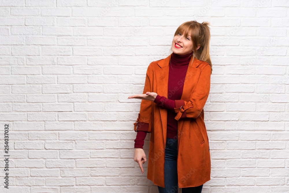 Woman with coat over white brick wall presenting an idea while looking smiling towards Woman with coat over white brick wall presenting an idea while looking smiling towards