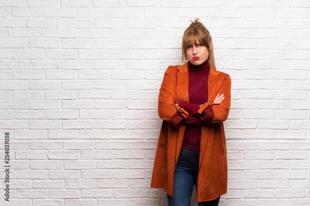 Woman with coat over white brick wall feeling upset Woman with coat over white brick wall feeling upset