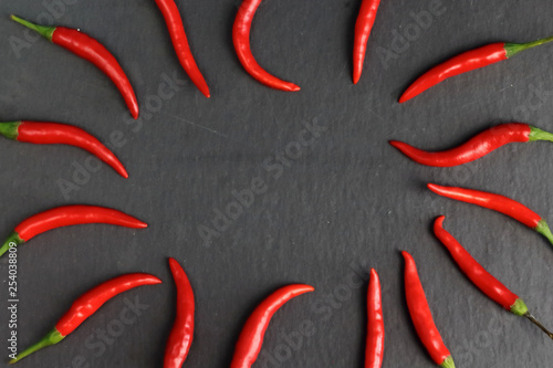 Frame of sharp hot spice red chilli fresh cayenne pepper on a black graphite slate stone surface with free copy space for text. Natural vegeterian diet organic vegetable. Dark food foto