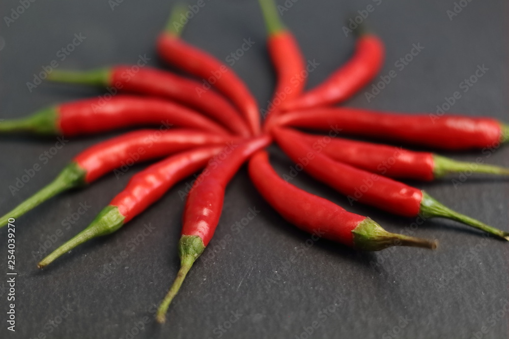 Group of sharp hot spice red chilli fresh cayenne pepper in the form of a circle of the sun  on a black graphite slate stone surface. Natural vegeterian diet organic vegetable. Dark food foto