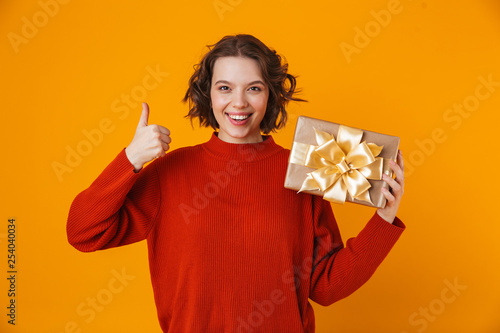 Emotional young pretty woman posing isolated over yellow wall background holding present gift. © Drobot Dean