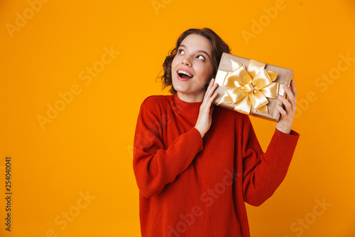Emotional young pretty woman posing isolated over yellow wall background holding present gift.