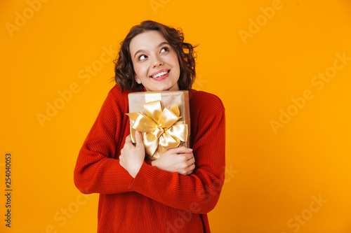 Emotional young pretty woman posing isolated over yellow wall background holding present gift. © Drobot Dean