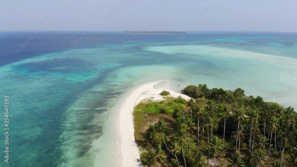 Wide aerial view from a drone approaching a tiny remote tropical island. A long strip of white sandy beach leads to tall palm trees covering the island. Paradise of Philippines. FORWARD, TILT DOWN. Wide aerial view from a drone approaching a tiny remote tropical island. A long strip of white sandy beach leads to tall palm trees covering the island. Paradise of Philippines. FORWARD, TILT DOWN.