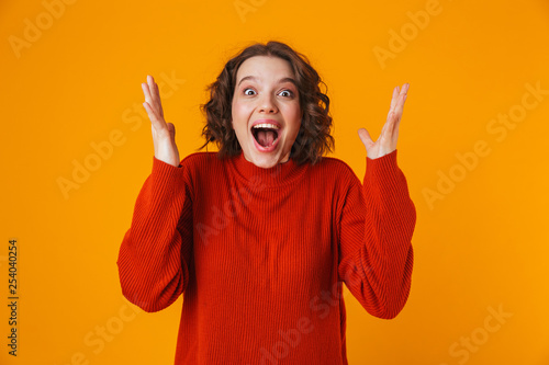 Excited emotional happy young pretty woman posing isolated over yellow wall background.
