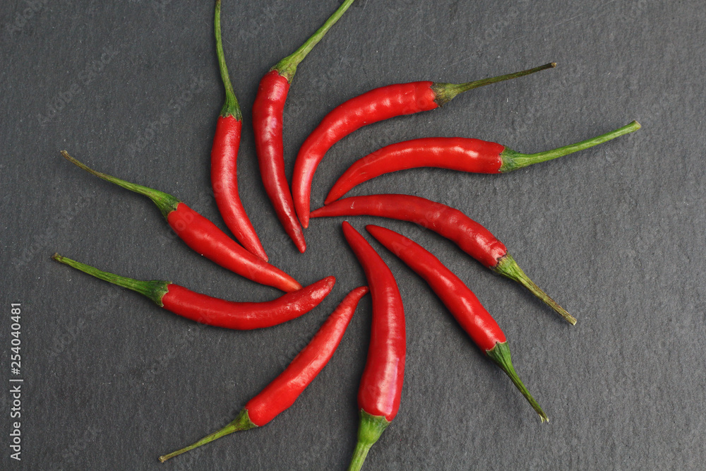 Group of sharp hot spice red chilli fresh cayenne pepper in the form of a circle of the sun  on a black graphite slate stone surface. Natural vegeterian diet organic vegetable. Dark food foto