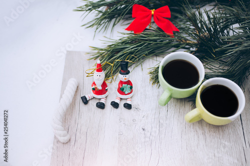 Two coffee cups and toy snowmen are standing at winter picnic outdoors. Pine tree and wooden tray on the snow in forest. Happy holidays time. Christmas decoration ornaments. Romantic celebration.