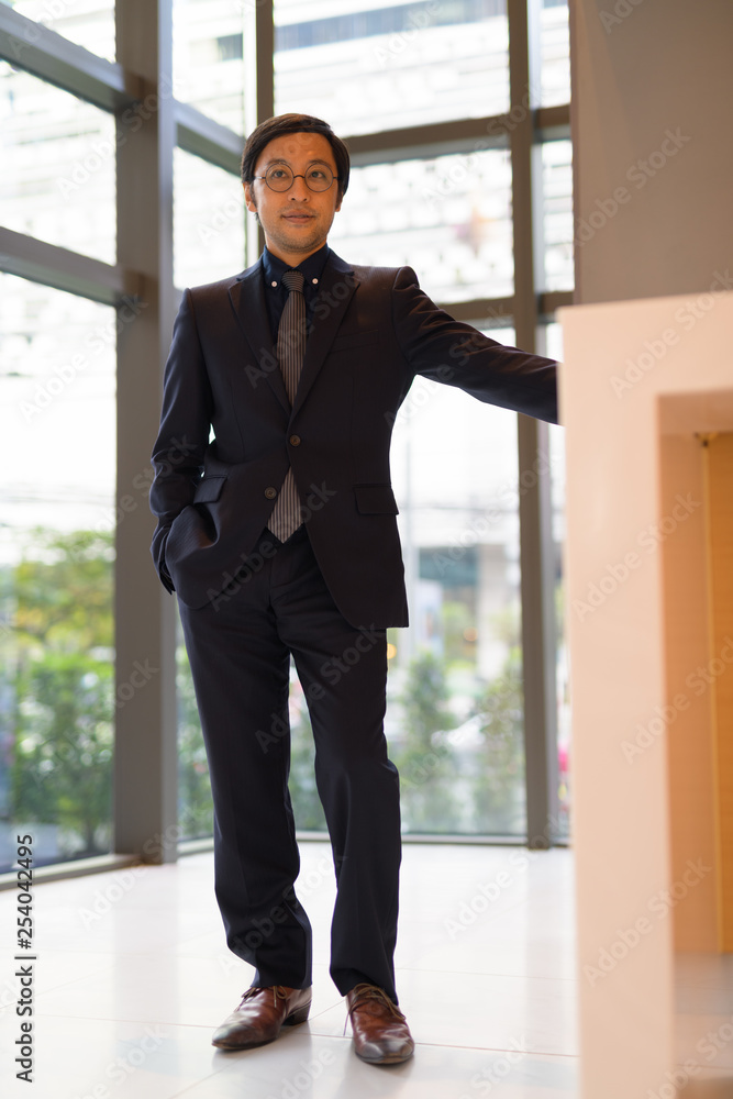 Full body shot of Asian businessman thinking by the window