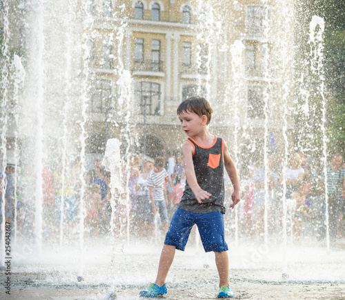 Fototapeta Naklejka Na Ścianę i Meble -  excited boy having fun between water jets, in fountain. Summer in the city
