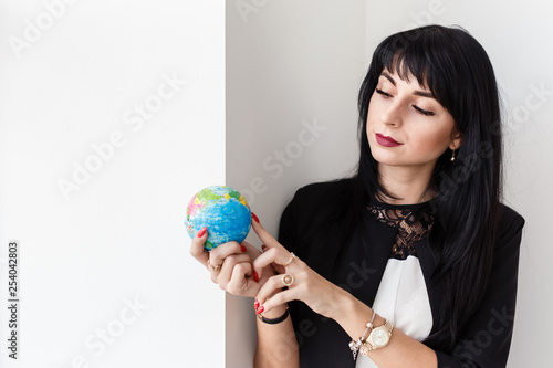 Young Beautiful smiling brunette woman dressed in a black business suit holding a globe of the planet Earth.