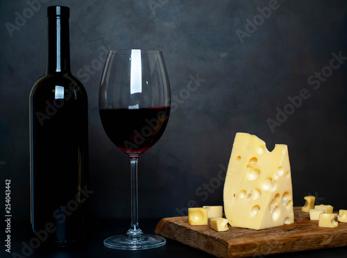 a bottle of wine, a wine glass with wine and delicious cheese on a cutting board, background stone