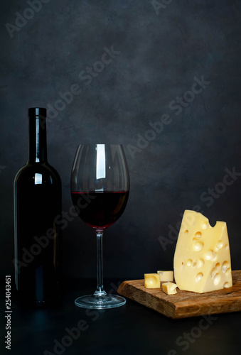 a bottle of wine, a wine glass with wine and delicious cheese on a cutting board, background stone