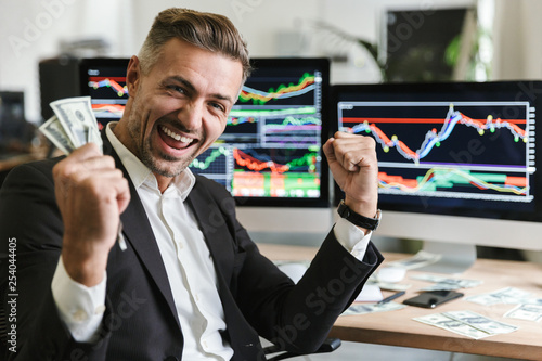 Photo of caucasian businessman rejoicing while working in office with digital graphics and charts