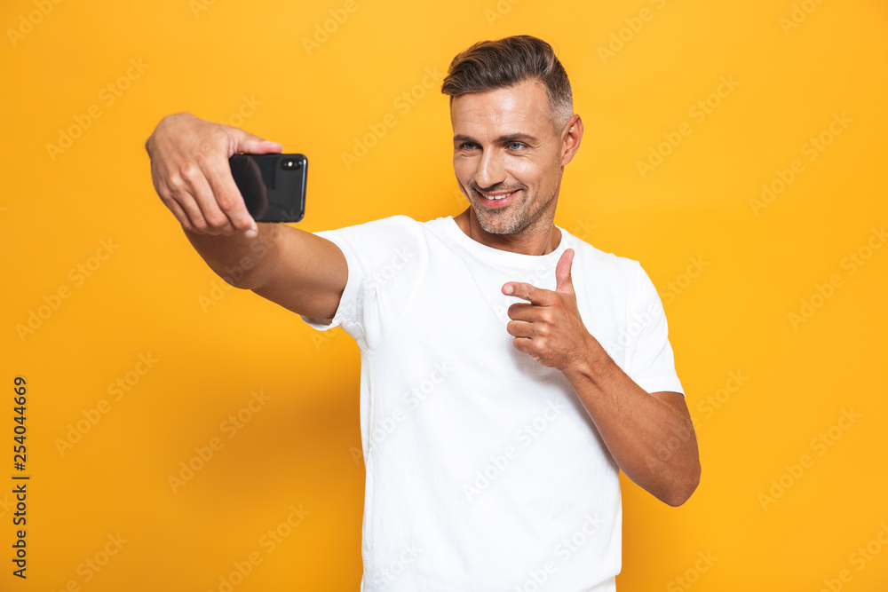 Image of happy man 30s in white t-shirt smiling and taking selfie photo on mobile phone isolated Image of happy man 30s in white t-shirt smiling and taking selfie photo on mobile phone isolated
