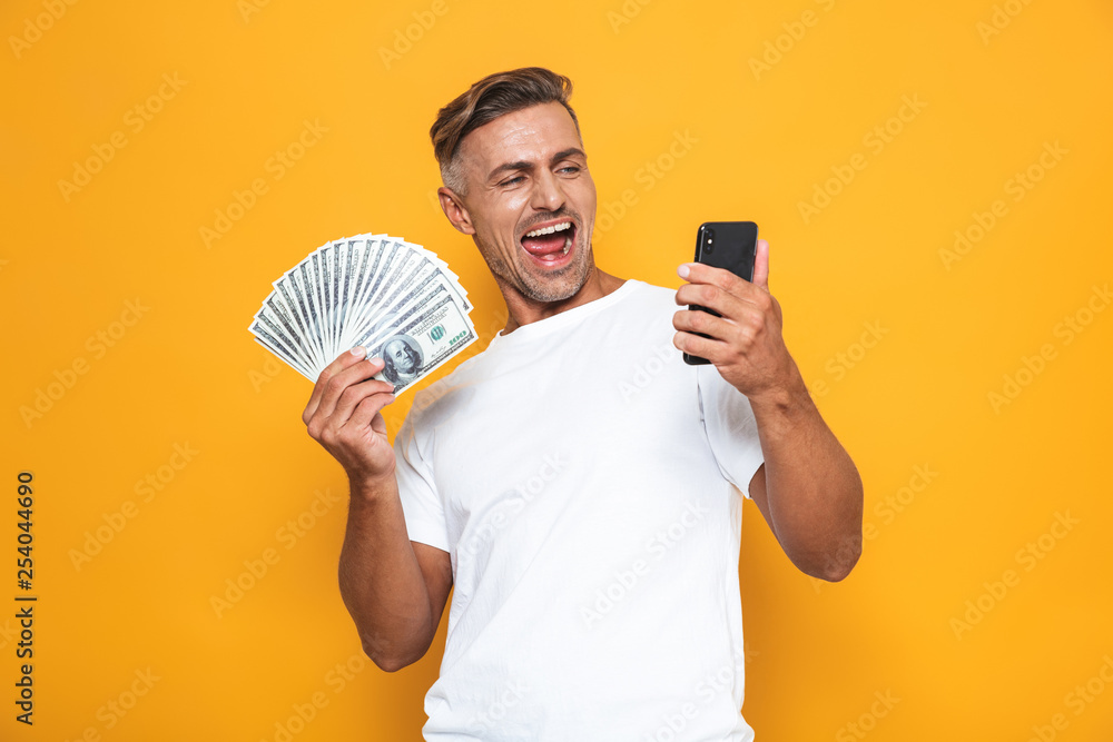 Image of brunette guy 30s in white t-shirt holding cell phone and bunch of money Image of brunette guy 30s in white t-shirt holding cell phone and bunch of money