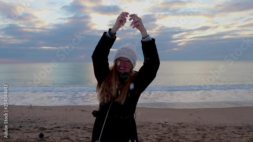 Adult woman rejoices in the snow on a sandy beach after a snowfall, against the backdrop of a calm sea.
