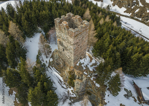 Aerial view of medieval tower ruins of fortess in forest. Stone tower on peak in Swiss alps with snow covered ground. photo