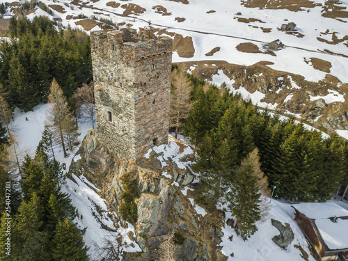 Aerial view of medieval tower ruins of fortess in forest. Stone tower on peak in Swiss alps with snow covered ground. photo