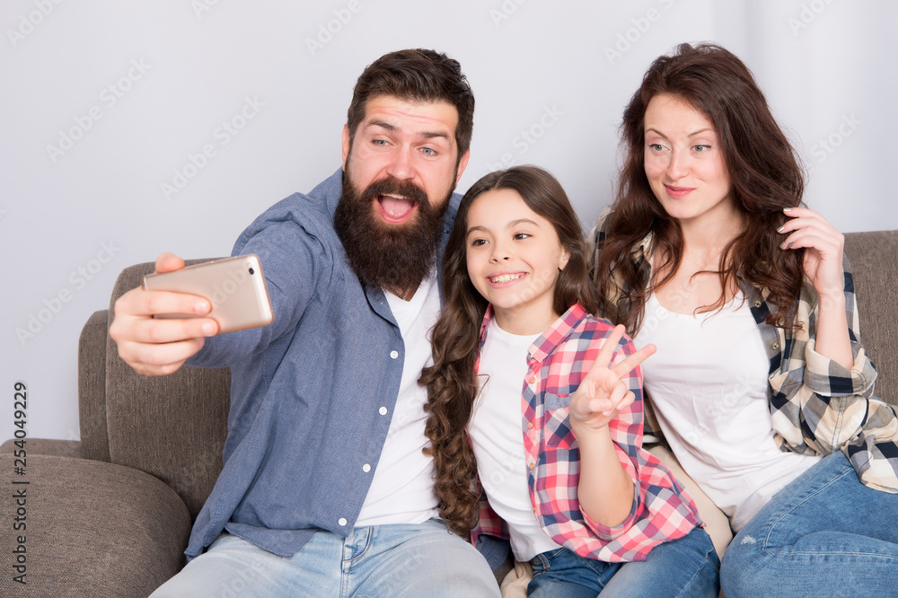 Use smartphone for selfie. Friendly family having fun together. Mom dad and daughter relaxing on couch. Family posing for photo. Capture happy moments. Family selfie. Family spend weekend together Use smartphone for selfie. Friendly family having fun together. Mom dad and daughter relaxing on couch. Family posing for photo. Capture happy moments. Family selfie. Family spend weekend together