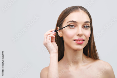 Young woman applying the black mascara on white