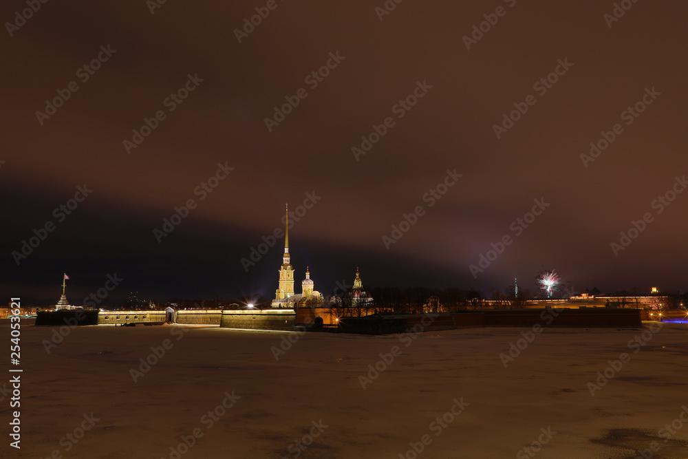 Peter and Paul Fortress of St. Petersburg, Russia in the evening or in the night and Neva river covered with the ice and snow in the cloudy weather an with the fireworks in the sky