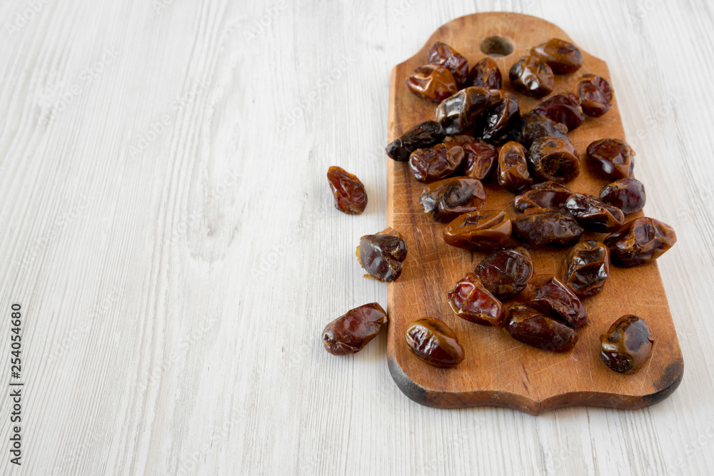 Obraz premium Dried dates on rustic wooden board over white wooden background, side view. Copy space.