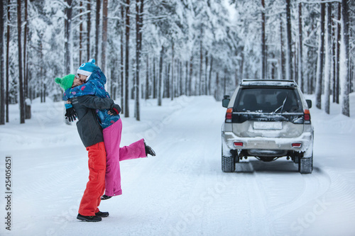 Happy loving couple kissing in the snowy winter forest, spending Christmas holidays together. Seasonal outdoor activities. car trip Capture lifestyle.