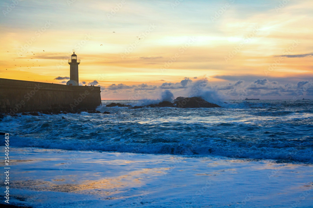 Seascape. The waves of the Atlantic Ocean crash against the rocks at sunset by the lighthouse. Lisbon, Portugal
