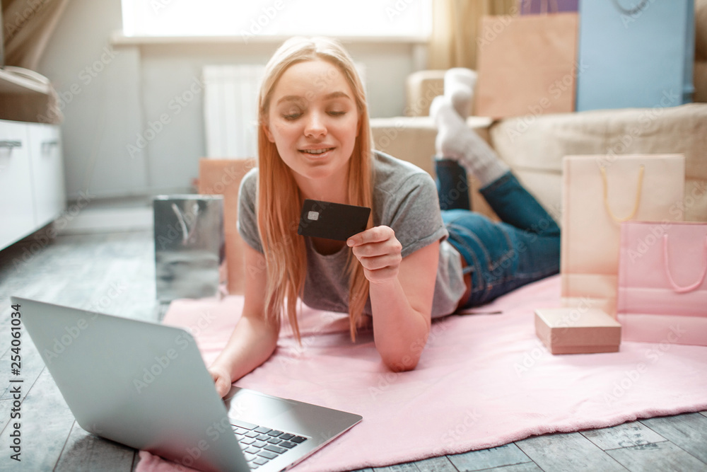 Online shopping at home. Young happy woman ia ready to spend money from husband's bank card on black Friday while lying on the floor with shopping bags Online shopping at home. Young happy woman ia ready to spend money from husband's bank card on black Friday while lying on the floor with shopping bags