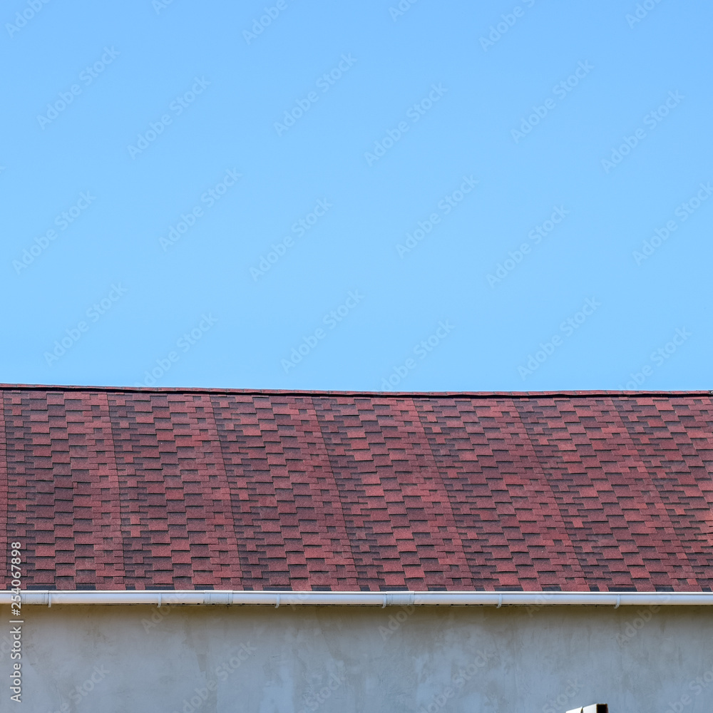 Roof from multi-colored bituminous shingles. Patterned bitumen shingles. Bituminous burgundy roof.