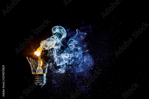 Сosmic explosion of burning light bulb with flying splinters of broken glass and smoke on isolate black background. Сoncept of creative art of starry sky, cosmos,  universe and the big bang theory.