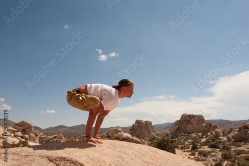 Young adult man playing with advanced yoga poses in the desert,. Urdhva Kukkutasana posture.  photo