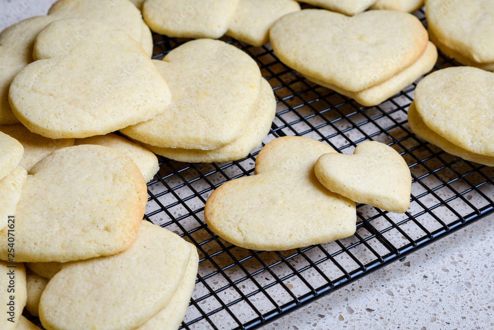 Stacks of heart shaped sugar cookies on a black wire cooling rack, granite kitchen counter