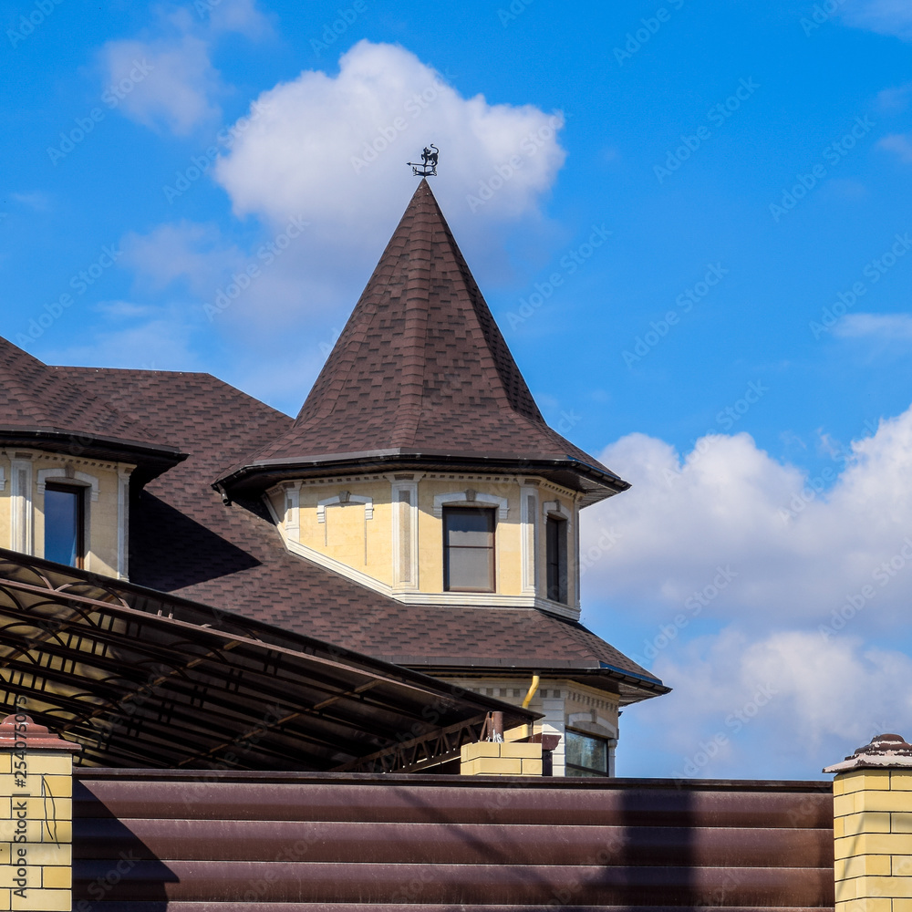 Decorative metal on the roof of a brick house. Fence made of corrugated metal.