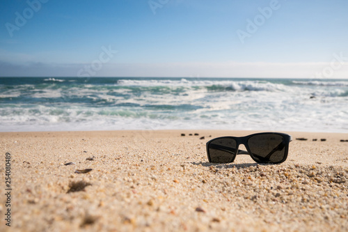 Sunglasses on beach, sunny summer day. Copy space on left.