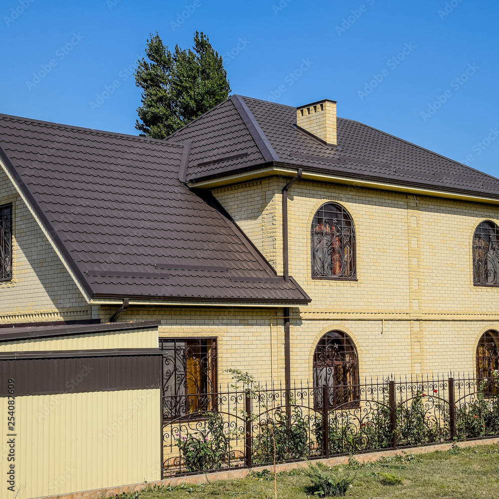 House of yellow brick and brown corrugated roof made of metal. Lattices ...