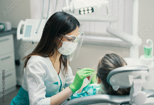 Female Dentist checking little cute girl patient at dental clinic. She is inspecting her mouth.