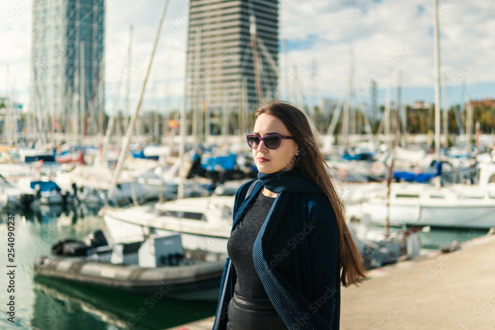 Businesswoman in sunglasses walking with a lot of yachts and boats behind.