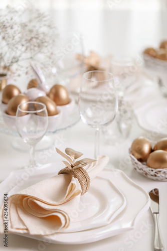 Happy Easter! Golden decor and table setting of the Easter table with white dishes of white color.