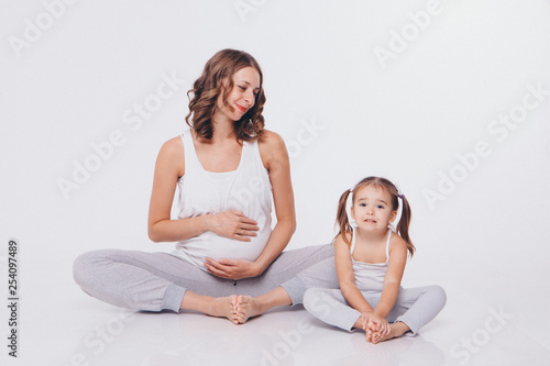 international women day: pregnant woman and little girl in tracksuits sitting on the floor on white background