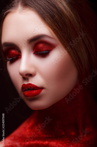 Red makeup in the style of beauty. Bright lips and eyes. Portrait of a beautiful young girl. Journal detailed skin retouching. Expressive eyebrows. Huge eyelashes. Neon shadows. © INTHEBLVCK